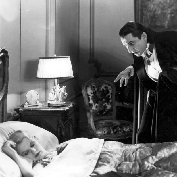 Bela Lugosi als Graf Dracula steht über einer schlafenden Frau im Film „Dracula“ (1931).