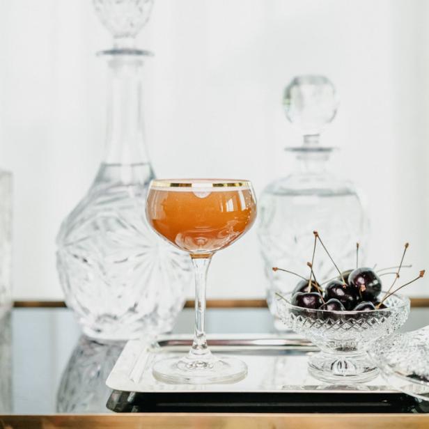 Ein Cocktail in einem Kristallglas steht neben Kirschen und Karaffen auf einem Serviertablett.