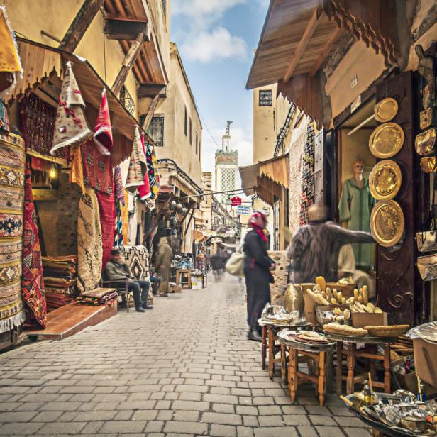 Eine belebte Gasse mit Geschäften und einer Moschee im Hintergrund.