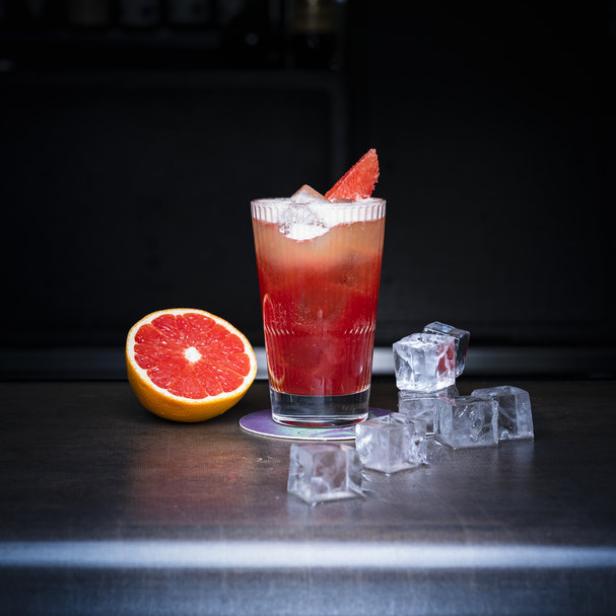 Ein Glas mit einem roten Cocktail, Eiswürfeln und einer halben Grapefruit auf einer Bar.