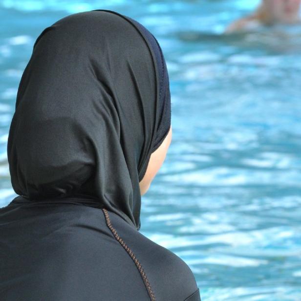 Eine Frau mit Burqini steht am Beckenrand und blickt auf das Wasser.