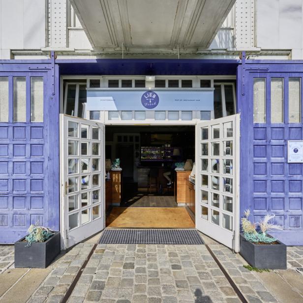 Der Eingang zum Restaurant „Lieb & Fisch“ mit blauen Schiebetüren und geöffneten weißen Fenstertüren.