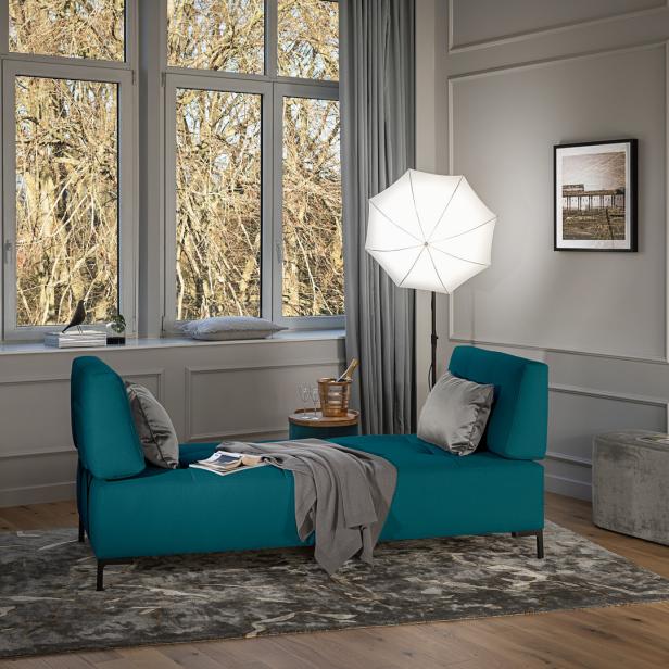 Ein türkisfarbenes Sofa mit Kissen in einem eleganten Wohnzimmer mit grauen Wänden und einem großen Fenster.