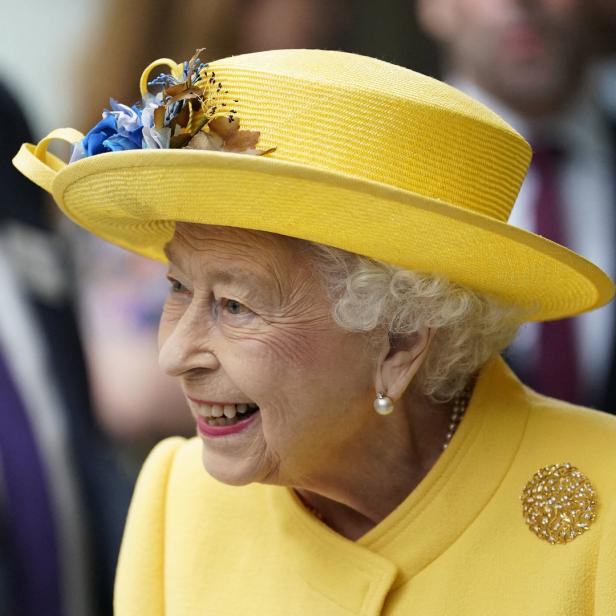 Königin Elisabeth II. lächelt in einem gelben Hut und Blazer.