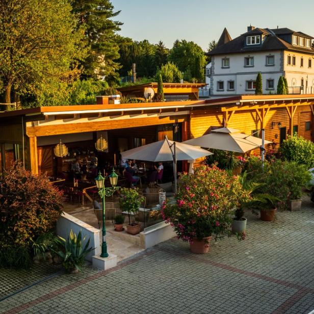 Ein Restaurant mit Gästen im Außenbereich und einem Parkplatz im Hintergrund.