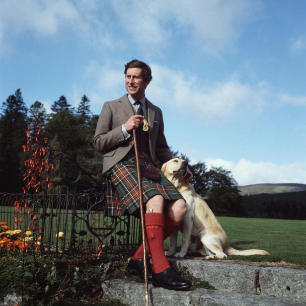 Prinz Charles sitzt mit seinem Labrador auf einer Bank im schottischen Hochland.
