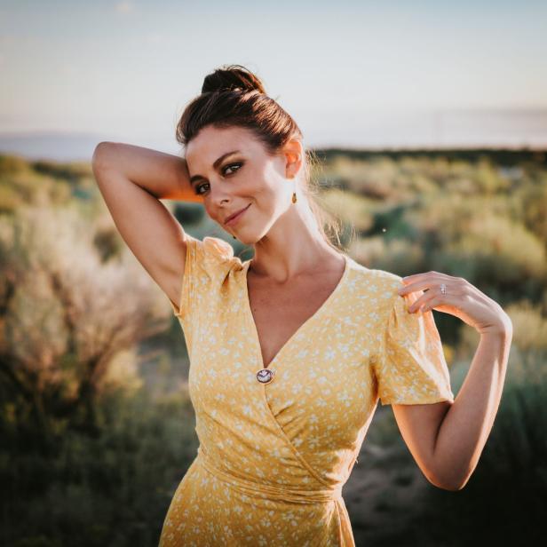 Eine Frau in einem gelben Kleid posiert in einer Landschaft.