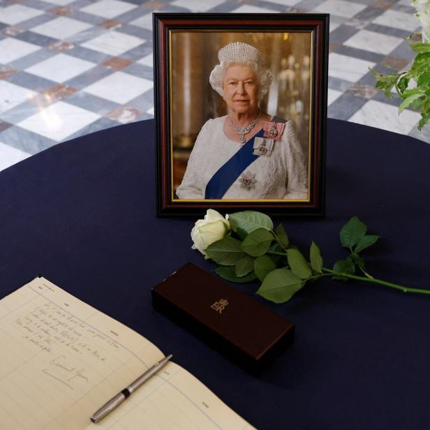 Ein Porträt von Königin Elisabeth II. steht auf einem Tisch neben einem Kondolenzbuch, einer Rose und einem Blumenstrauß.