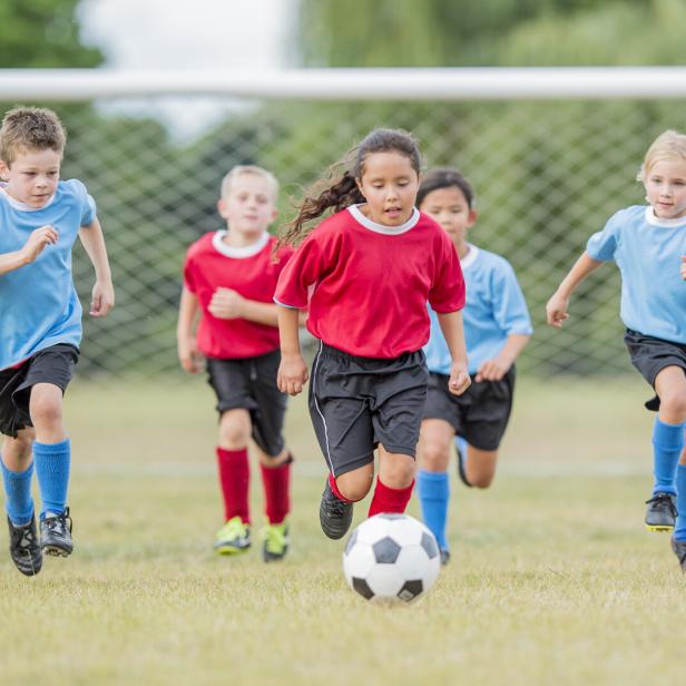 Fünf Kinder spielen Fußball auf einem Rasenplatz und rennen zum Ball.