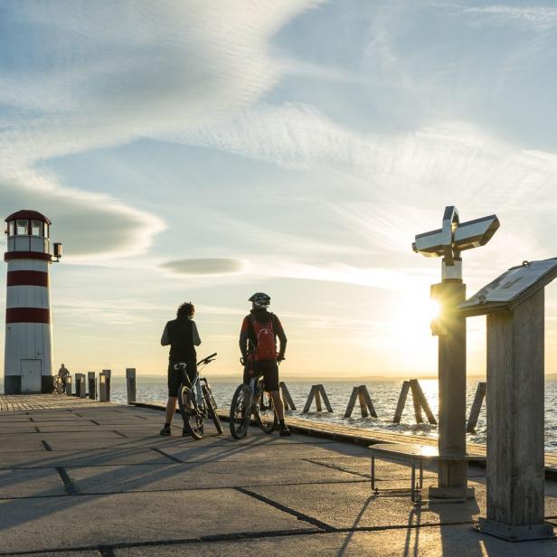 Zwei Radfahrer stehen auf einem Pier mit Blick auf einen See bei Sonnenuntergang.