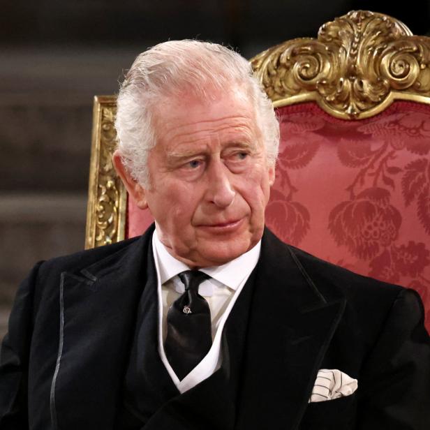 König Charles III. sitzt auf einem verzierten roten Stuhl.