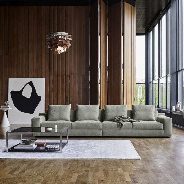 Ein Wohnzimmer mit einem grauen Sofa, einem Couchtisch und einem großen Fenster.
