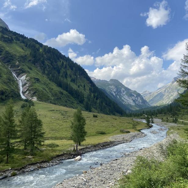 Ein Fluss schlängelt sich durch eine grüne Berglandschaft mit einem Wasserfall an einem Hang.