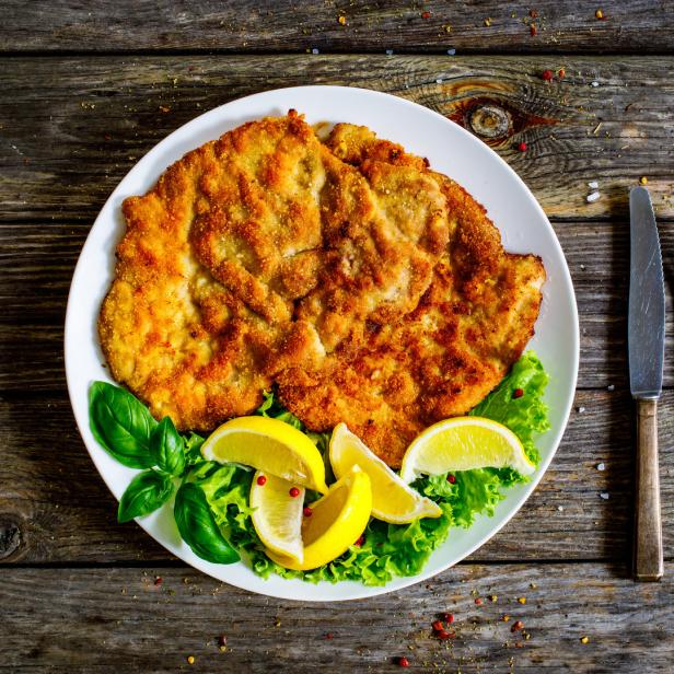 Ein Wiener Schnitzel mit Zitrone und Salat auf einem Teller.