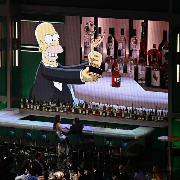 Homer Simpson hält eine Emmy-Trophäe vor einer Bar mit unzähligen Flaschen.