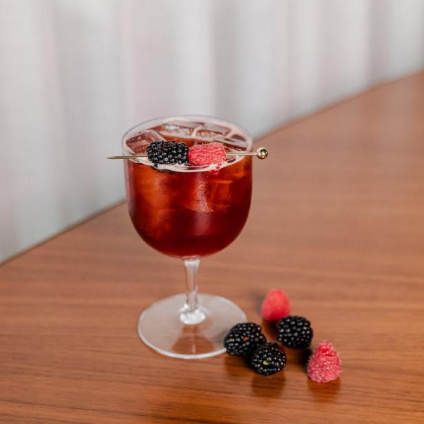 Ein Cocktail mit Brombeeren und Himbeeren auf einem Holztisch.