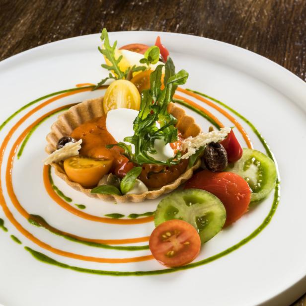 Ein Tomaten-Tarte mit Mozzarella und Rucola auf einem Teller mit Dekoration.