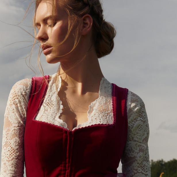 Eine Frau mit geschlossenen Augen trägt ein Dirndl vor einem bewölkten Himmel.