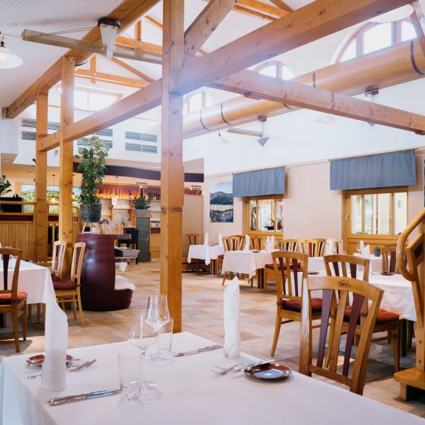 Ein helles Restaurant mit Holzbalken und gedeckten Tischen.