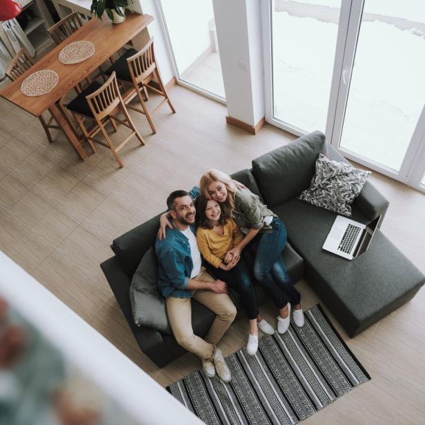 Eine Familie sitzt zusammen auf einem Sofa in einem hellen Wohnzimmer.