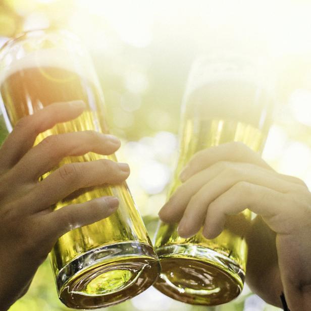 Zwei Personen stoßen mit Biergläsern im Freien an.