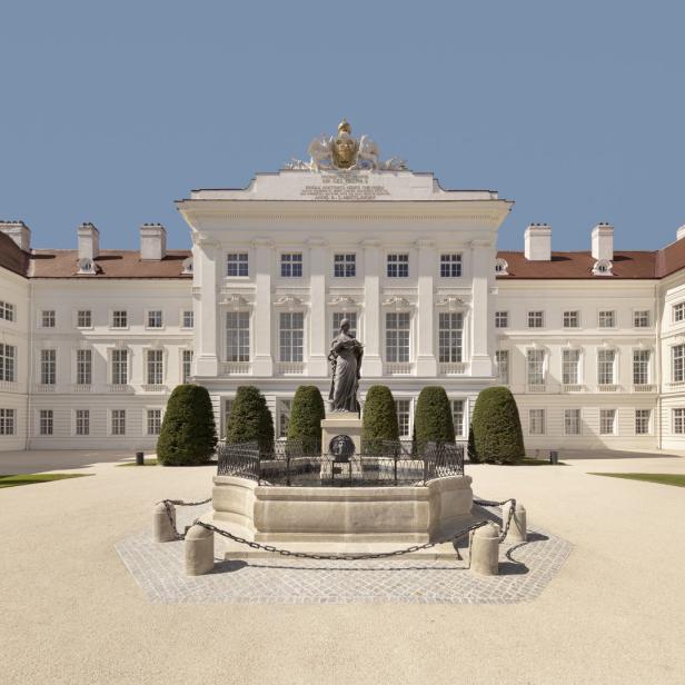 Das Schloss Hof mit einem Brunnen und einer Statue im Vordergrund.