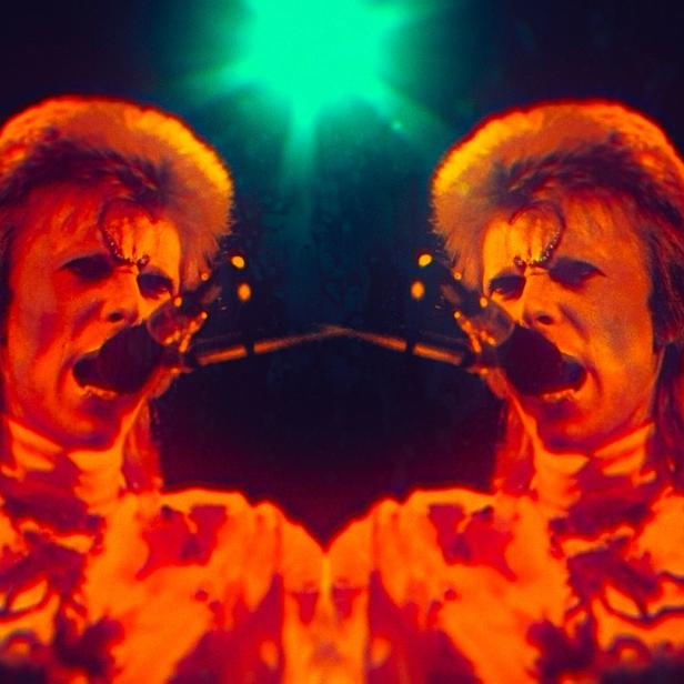 Ein verzerrtes Doppelbild von David Bowie, der in ein Mikrofon singt.