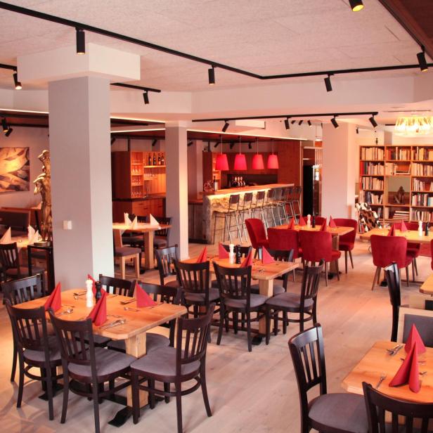 Ein einladendes Restaurant mit Holztischen, roten Akzenten und einer Bar im Hintergrund.