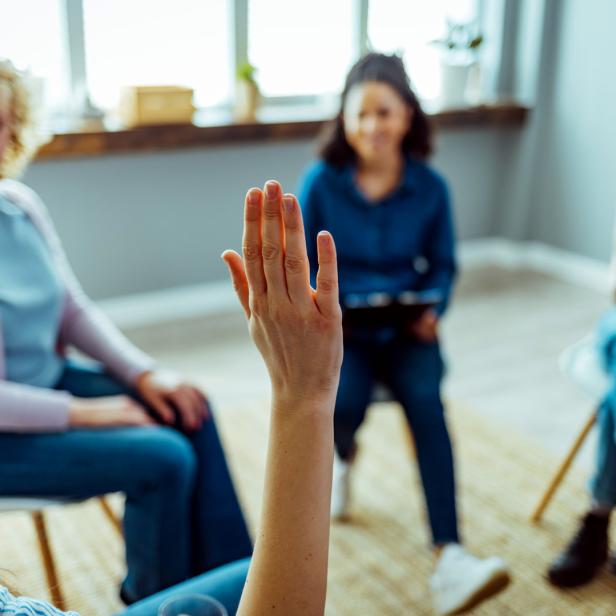 Eine Frau hebt die Hand in einer Gruppensitzung.