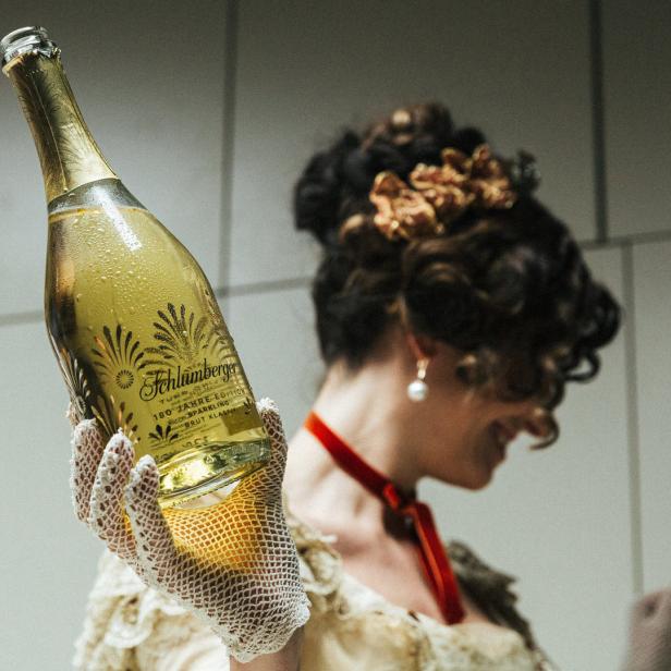 Eine Frau im historischen Kleid präsentiert eine Flasche Schlumberger Sekt.