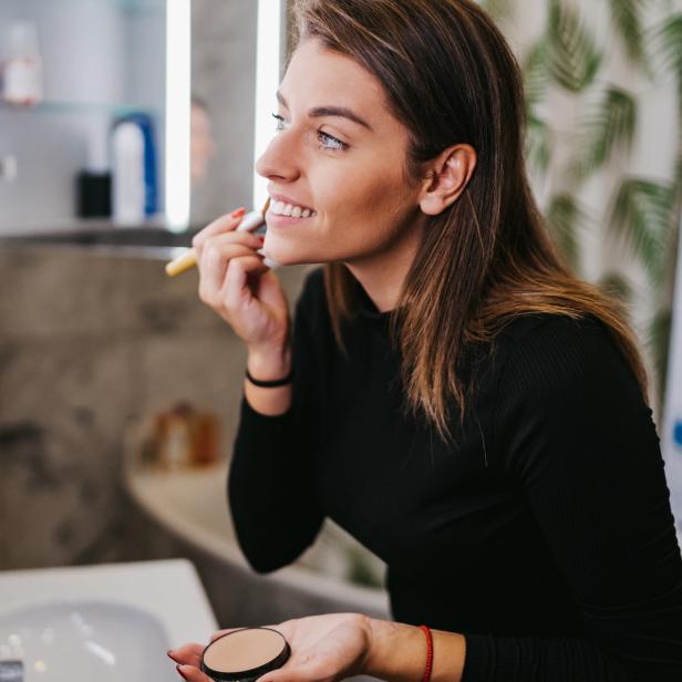 Eine Frau trägt Make-up vor einem Spiegel im Badezimmer auf.