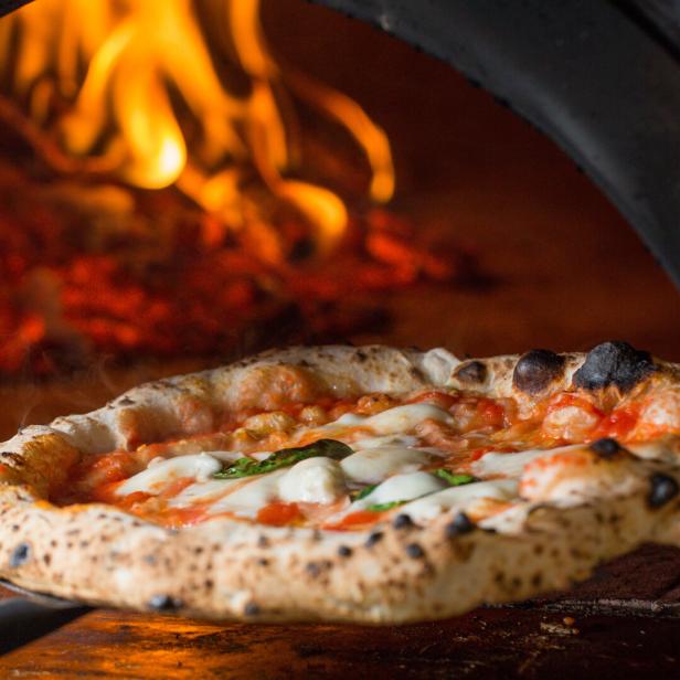 Pizza wird aus dem Steinofen geholt.