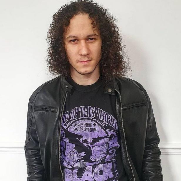 Ein Mann mit lockigem Haar trägt ein „Black Sabbath“-T-Shirt und eine Lederjacke.