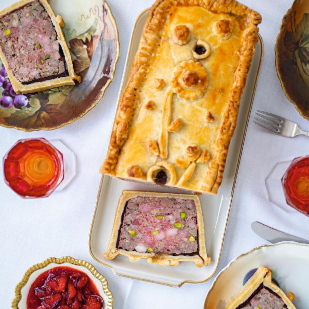 Ein dekorativer Pastetenkuchen mit Füllung und Beilagen auf einem Tisch.