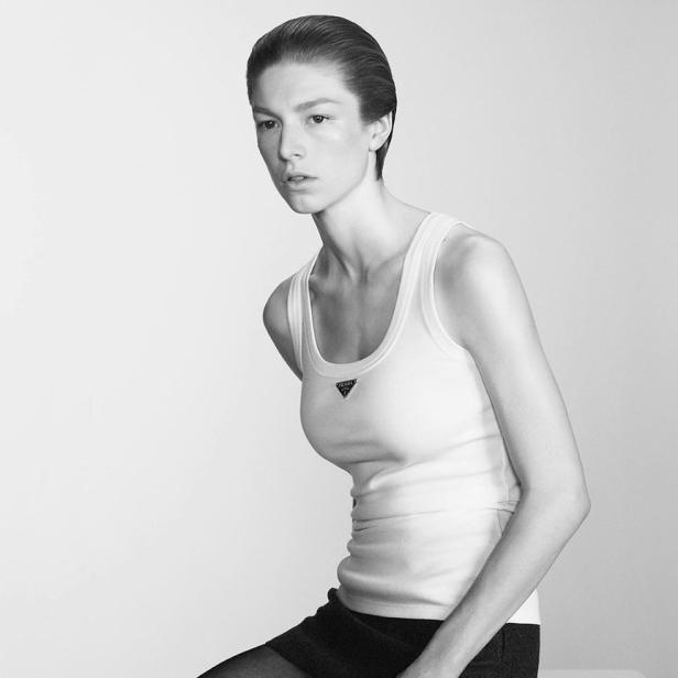 Eine Frau mit kurzem, dunklem Haar trägt ein weißes Tanktop von Prada und einen schwarzen Rock.