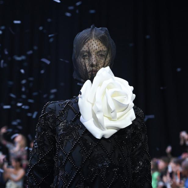 Ein Model mit Schleier und einer großen weißen Rose auf einem verzierten schwarzen Kleid.