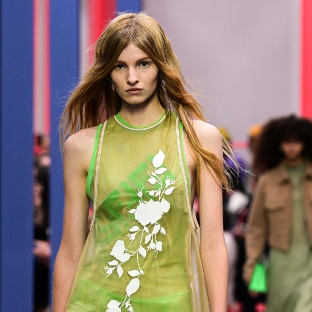 Eine Frau mit blonden Haaren trägt ein grünes Kleid mit weißen Blumen auf einem Laufsteg.