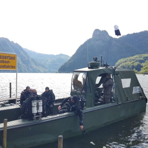 Taucher steigen an einem See in ein Boot mit der Aufschrift „Wassertaxi, Speedboot-Rundfahrten“.