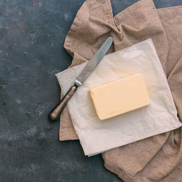 Ein Stück Butter liegt mit einem Messer auf einem Küchentuch.