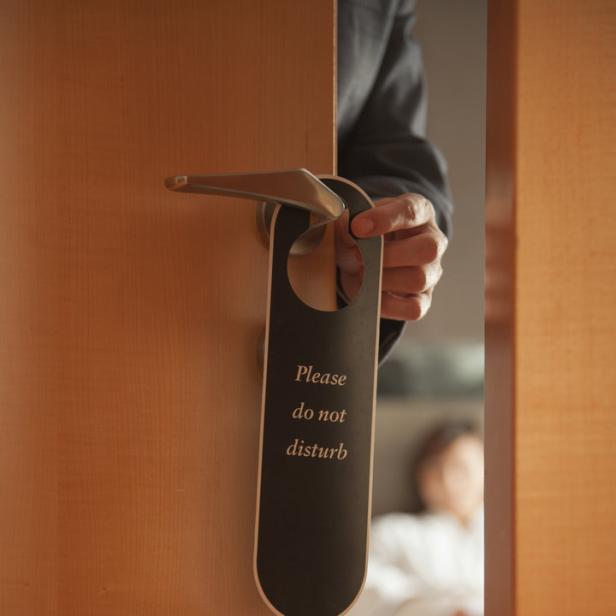 Eine Hand hängt ein „Bitte nicht stören“-Schild an eine Hotelzimmertür.