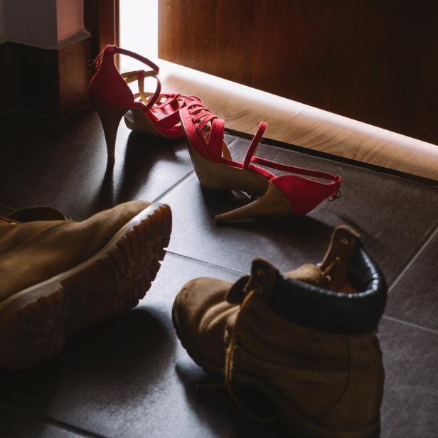 Ein Paar rote High Heels und braune Stiefel stehen auf dem Boden vor einer Tür.