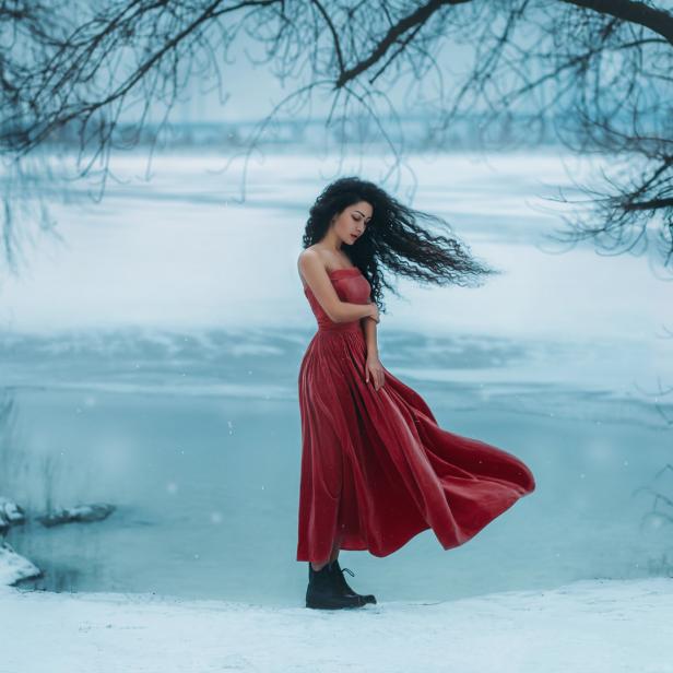 Eine Frau in einem roten Kleid steht im Schnee an einem See.