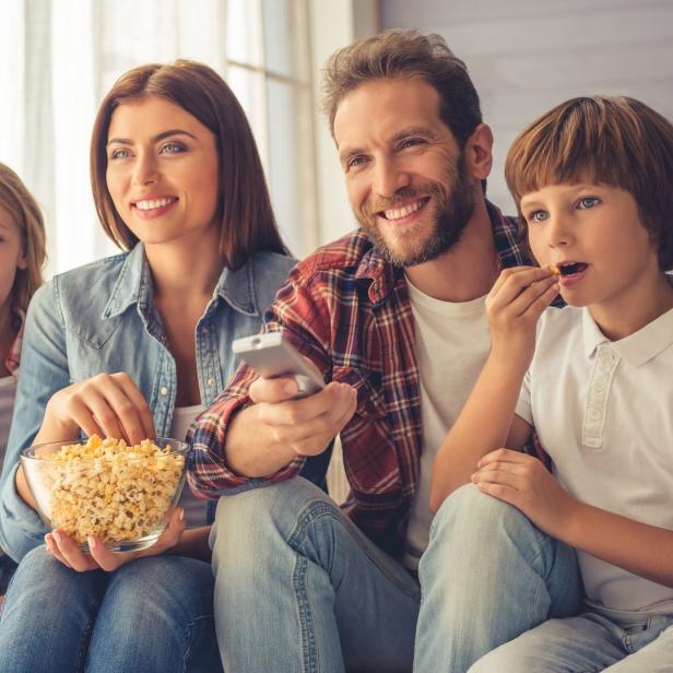 Eine Familie sitzt auf dem Sofa und isst Popcorn, während sie fernsieht.