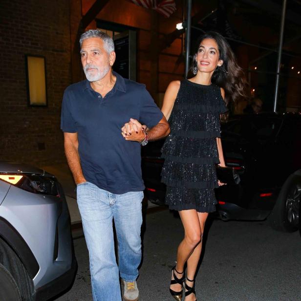 George und Amal Clooney verlassen händchenhaltend ein Gebäude.