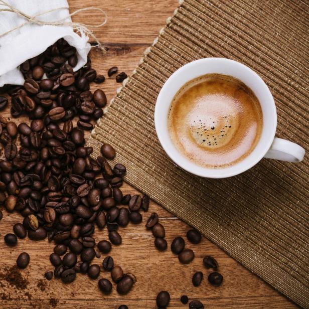 Kaffeetasse mit Siebträger und ganzen Bohnen daneben.