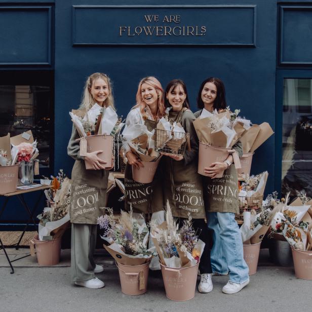 Vier Floristinnen stehen vor ihrem Blumengeschäft „Flowergirls“ und halten Blumensträuße.