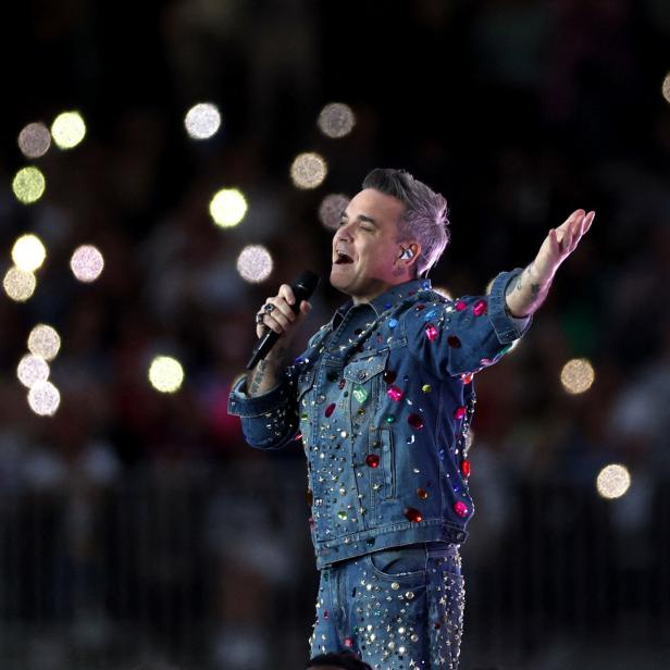 Robbie Williams tritt in einer mit bunten Juwelen besetzten Jeansjacke auf einer Bühne auf.