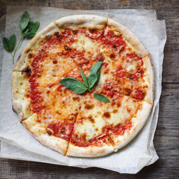Eine Pizza Margherita mit Basilikum auf einem Holztisch.