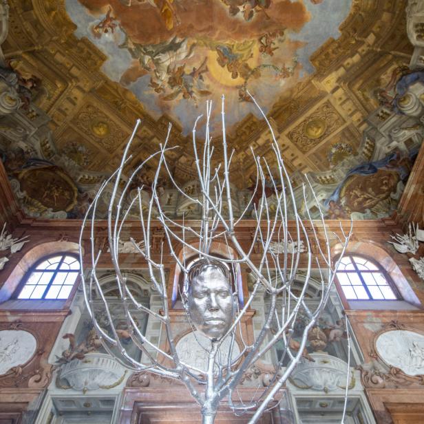 Eine silberne Skulptur eines Kopfes in einem Raum mit einem kunstvollen Deckengemälde.