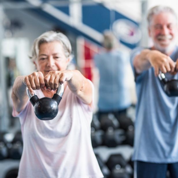 Ein älteres Paar macht gemeinsam Krafttraining und hebt Kettlebells hoch.